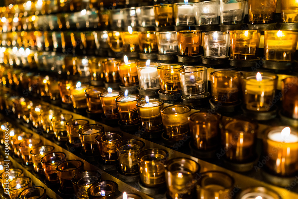Macro closeup of many yellow candles with flame in church, rows of flame