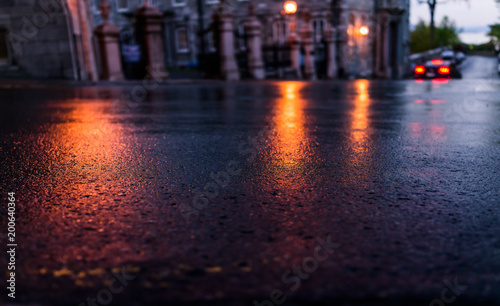 Macro closeup of wet street pavement at night with reflection of golden lantern lights background asphalt