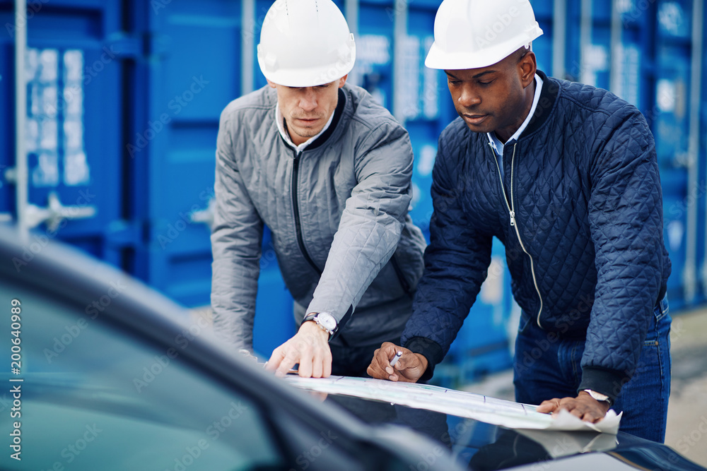 Two engineers standing in a commercial shipping yard discussing Two engineers standing in a commercial shipping yard discussing