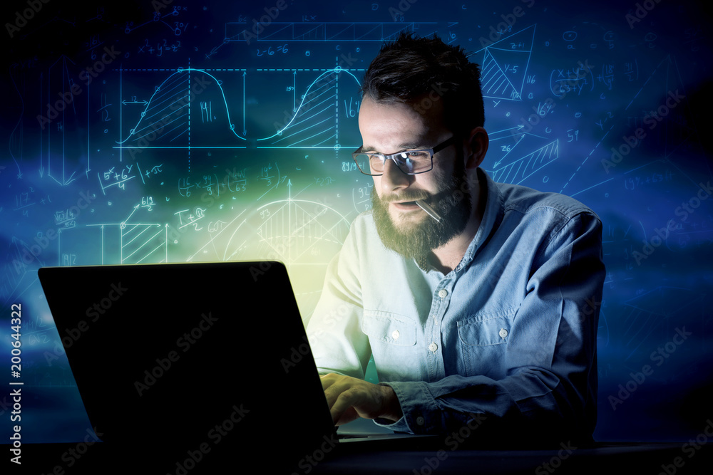 Young handsome businessman working late at night in the office with blue mathematic charts in the background Young handsome businessman working late at night in the office with blue mathematic charts in the background