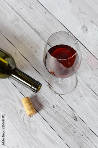 Red wine in a glass and a bottle on a light wooden table