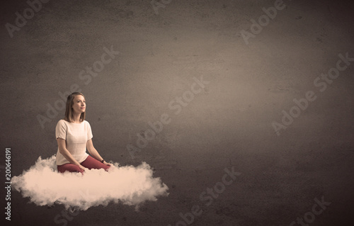 Caucasian woman sitting on a white fluffy cloud daydreaming beside a plain grunge background