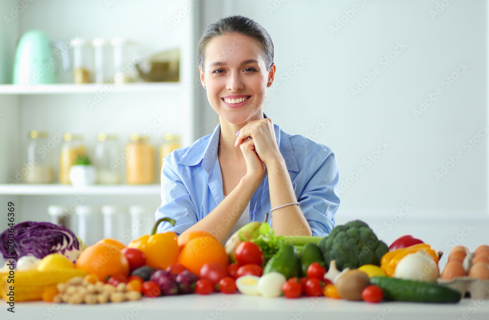 Young and cute woman sitting at the table full of fruits and vegetables in the wooden interior