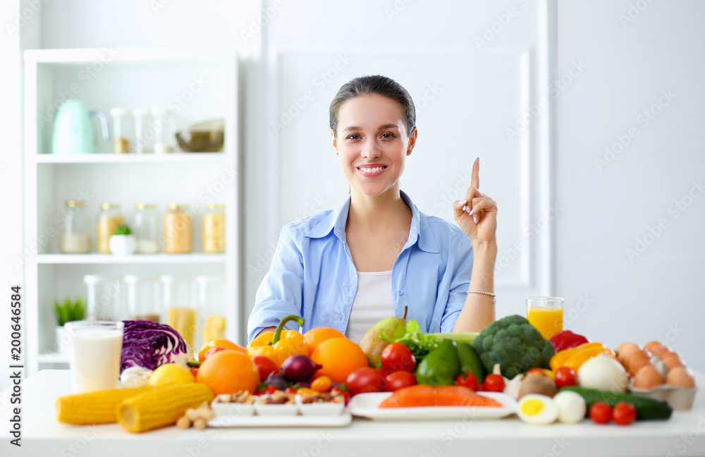 Young and cute woman sitting at the table full of fruits and vegetables in the wooden interior