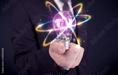 A classy businessman holding a colorful light bulb with shining circles in front of dark background concept.
