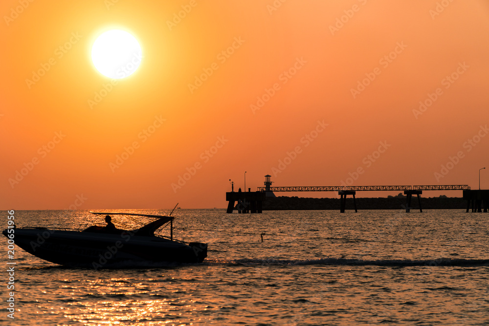 A boat is going out from port while the sun is going down to the ocean with port and jetty background..Sunset. Travel concept. What's your dream?