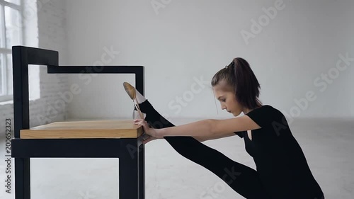 Cute slim girl doing stretching legs sitting in studio indoors. Attractive gymnast training flexibility, girl increases elasticity of muscles and improves mobility of joints. Proper stretching photo