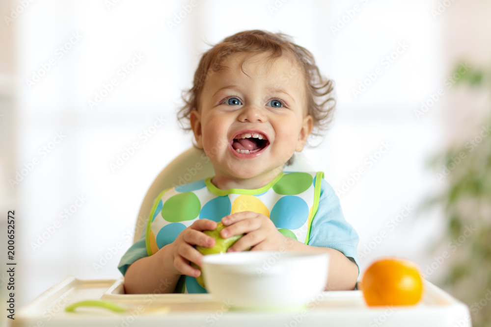 Cute baby child eating healthy food. Portrait of happy kid boy with bib in high chair. Cute baby child eating healthy food. Portrait of happy kid boy with bib in high chair.