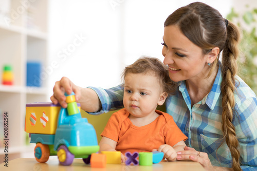 Curly child boy and young woman playing with developmental toy in daycare or kindergarten
