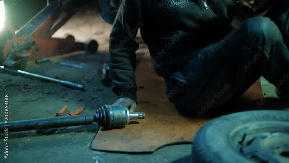 The mechanic in dirty auto repair shop repairs the car - repairs constant-velocity universal ball joint Shrus and replaces a wheel The mechanic in dirty auto repair shop repairs the car - repairs constant-velocity universal ball joint Shrus and replaces a wheel