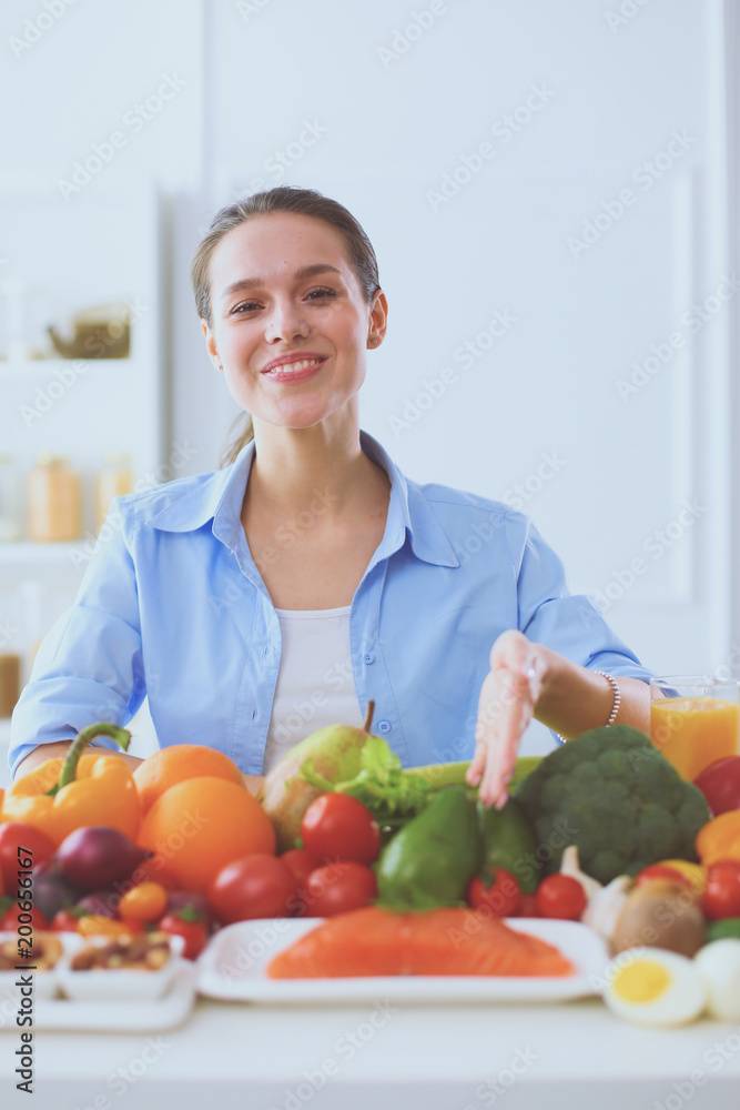 Young and cute woman sitting at the table full of fruits and vegetables in the wooden interior Young and cute woman sitting at the table full of fruits and vegetables in the wooden interior