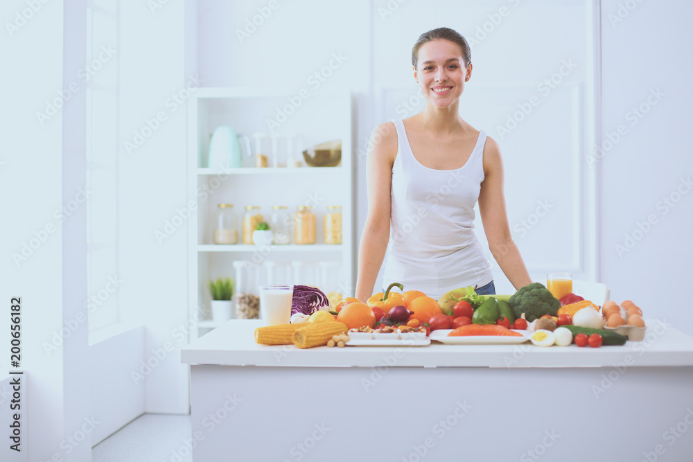 Young and cute woman sitting at the table full of fruits and vegetables in the wooden interior Young and cute woman sitting at the table full of fruits and vegetables in the wooden interior