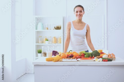 Young and cute woman sitting at the table full of fruits and vegetables in the wooden interior