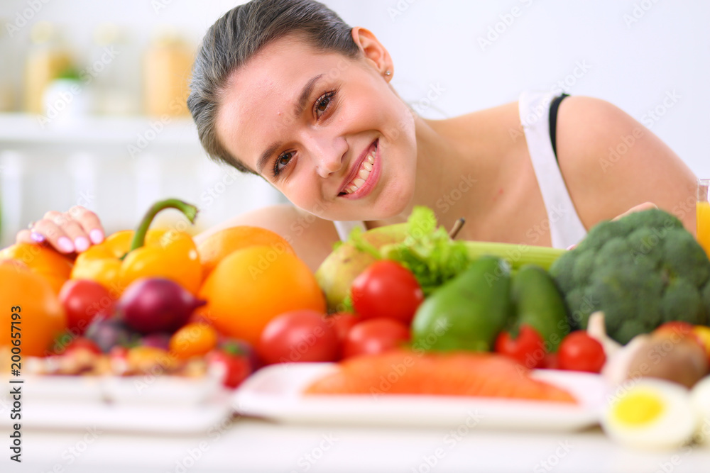 Young and cute woman sitting at the table full of fruits and vegetables in the wooden interior Young and cute woman sitting at the table full of fruits and vegetables in the wooden interior