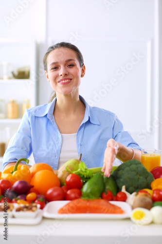 Young and cute woman sitting at the table full of fruits and vegetables in the wooden interior