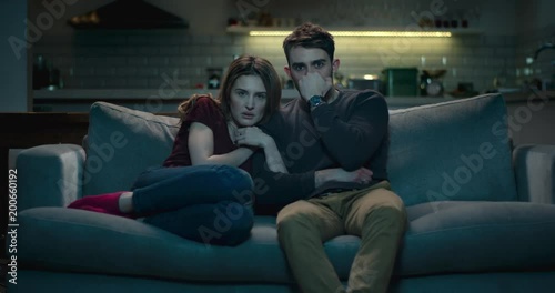 Frightened couple on a sofa late at night watching a scary horror film.