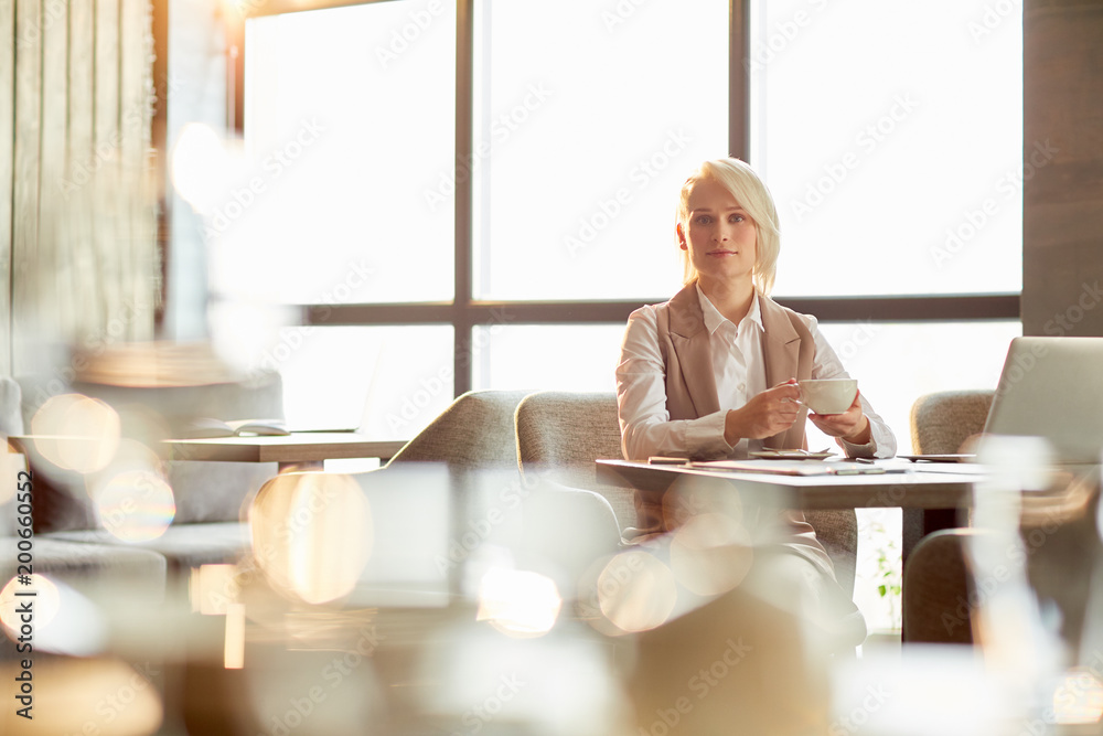 Young elegant woman with cup of tea or coffee sitting by table in cafe during coffee-break Young elegant woman with cup of tea or coffee sitting by table in cafe during coffee-break