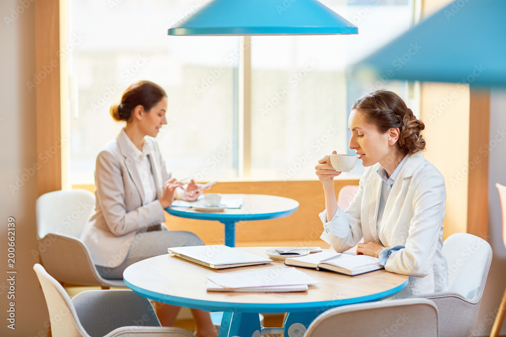 Young businesswoman drinking coffee from white porcelain cup while spending time in cafe Young businesswoman drinking coffee from white porcelain cup while spending time in cafe