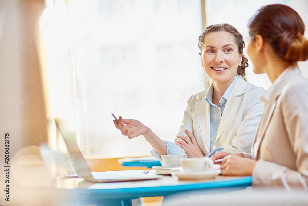 Happy young agent making presentation of her ideas or report in laptop while talking to colleague Happy young agent making presentation of her ideas or report in laptop while talking to colleague
