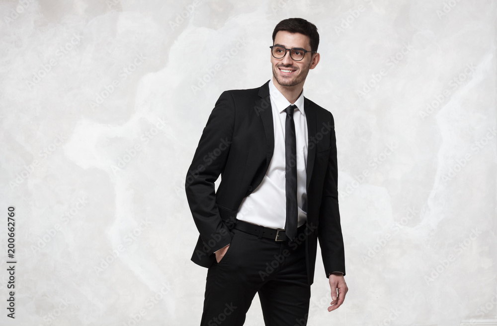 Elegant smiling young business man walking against grey texture wall Elegant smiling young business man walking against grey texture wall