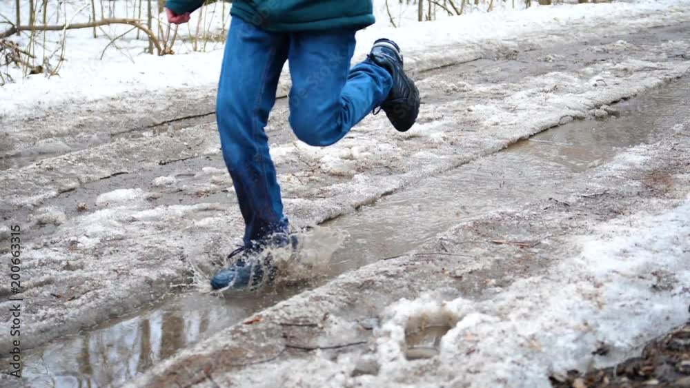 A child in the Park running on puddles. Splashes of water scatter on the parties. Entertainment, outdoor sports. Early spring. A child in the Park running on puddles. Splashes of water scatter on the parties. Entertainment, outdoor sports. Early spring.