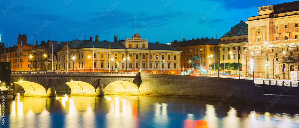 Stockholm Sweden. View Of Norrbro, Old Stone Arch Bridge Over Norrstrom Waterway With Lights Reflections In The Water Next To Royal Opera Building.