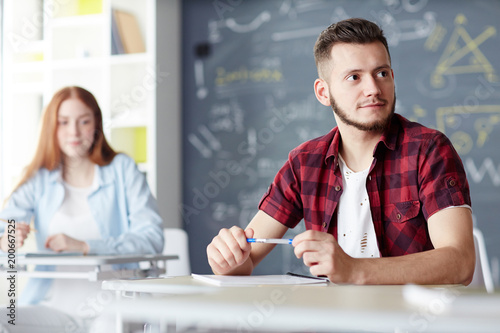 Student in casualwear looking at someone and listening to what he or she saying at lesson