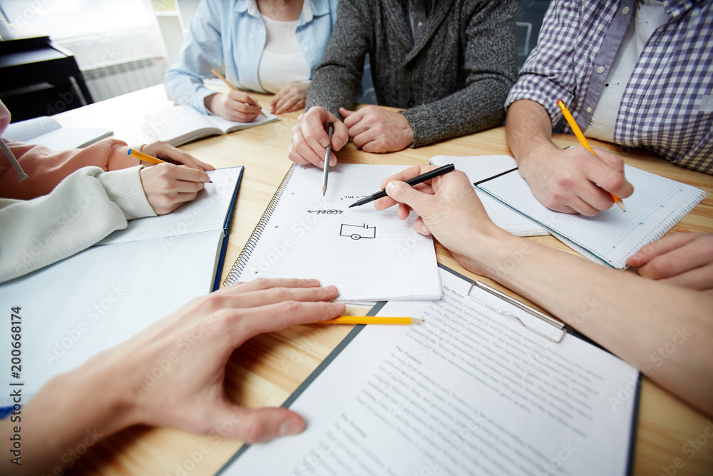 Student and teacher pointing at scheme of electric chain on paper while other people making notes Student and teacher pointing at scheme of electric chain on paper while other people making notes