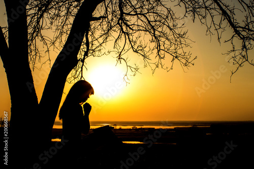 silhouette of woman praying to God in the nature witth the Bible at sunset, the concept of religion and spirituality
