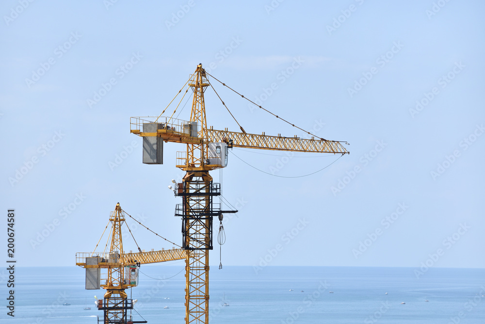 Two construction cranes on a sea background and a blue sky Two construction cranes on a sea background and a blue sky