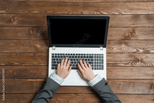 Top view of businesswoman sitting at wooden table and working with laptop