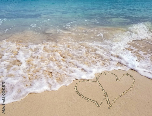 pair of hearts in beach sand with frothy ocean surf and turquoise ocean water