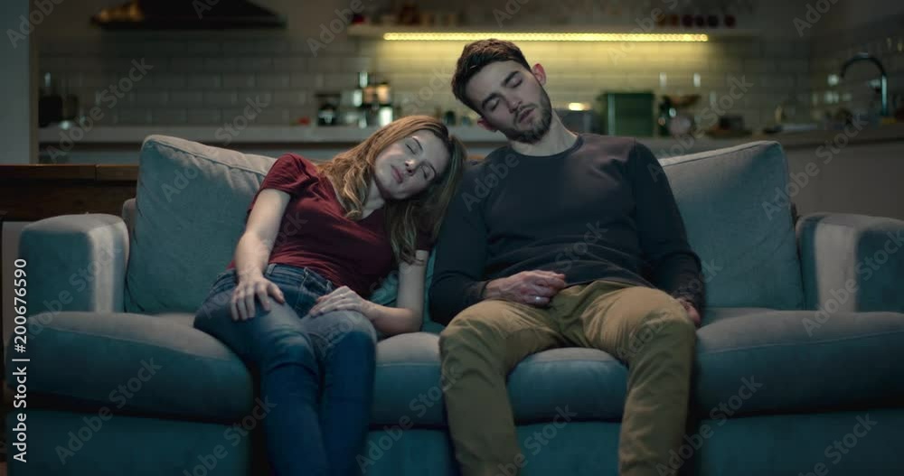 Tired and exhausted young couple asleep on the sofa after a long day.