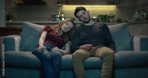 Tired and exhausted young couple asleep on the sofa after a long day.