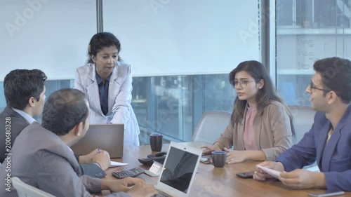 A ambitious attractive Indian woman or female boss is interacting with young mixed gender business team in modern office building. A motivated smiling businesswoman conducting meeting in boardroom. 