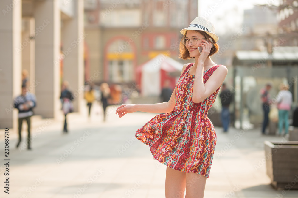 Naklejka premium Close-up of a smiling attractive girl with short hair talking on a mobile phone, standing on a street on a city street