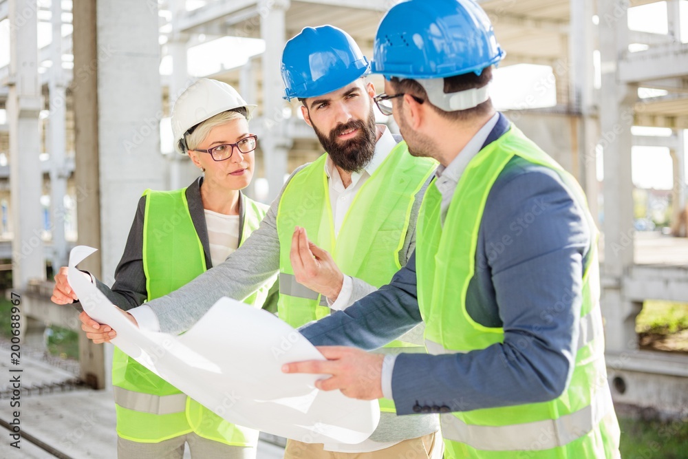 Mixed group of engineers or business partners at construction site, working together on building's blueprint. Architecture and teamwork concept. Mixed group of engineers or business partners at construction site, working together on building's blueprint. Architecture and teamwork concept.