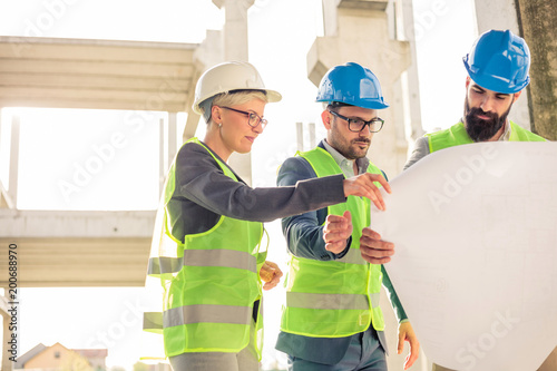 Obraz na płótnie Mixed group of engineers or business partners at construction site, working together on building's blueprint. Architecture and teamwork concept. w salonie