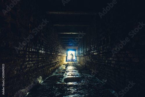 Silhouette of man with flashlight in dark dirty brick underground tunnel or sewerage corridor