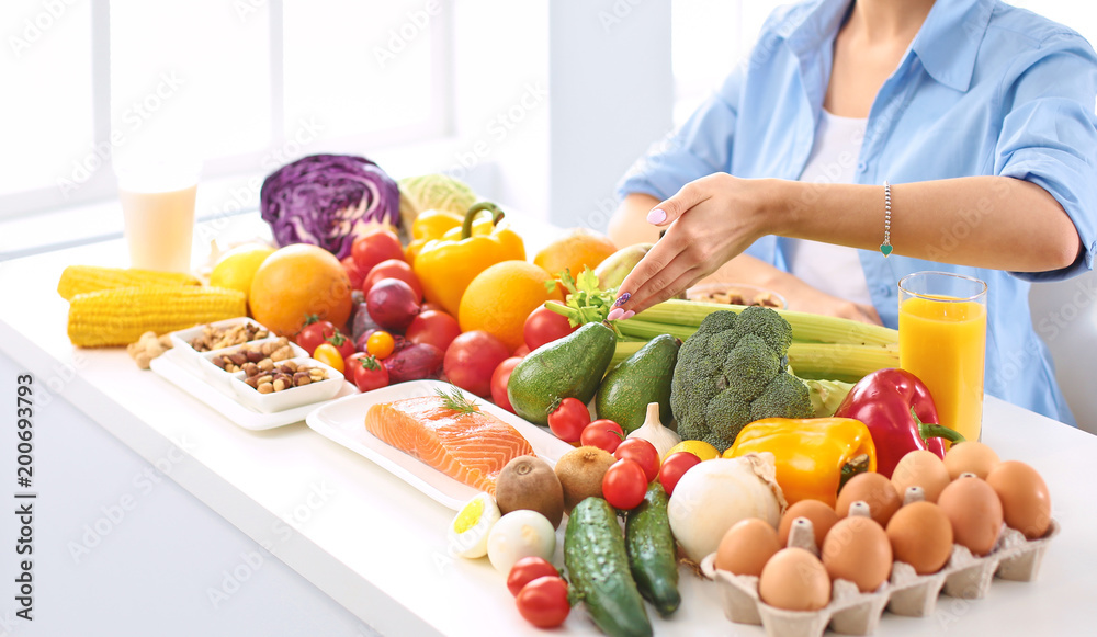 happy young housewife sitting in the kitchen preparing food from a pile of diverse fresh organic fruits and vegetables happy young housewife sitting in the kitchen preparing food from a pile of diverse fresh organic fruits and vegetables