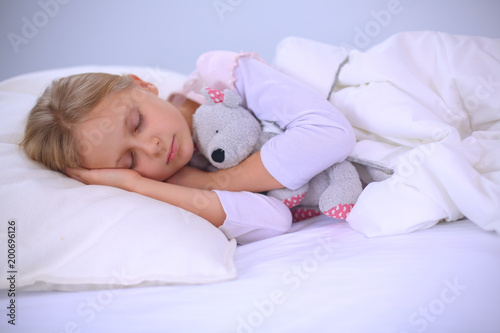 Child little girl sleeps in the bed with a toy teddy bear.