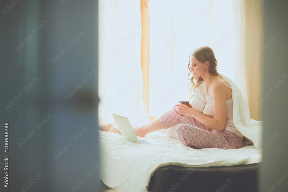 Young beautiful woman sitting in bed with laptop.