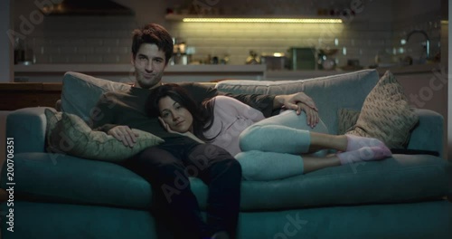 Happy couple relaxing on a comfy sofa in the evening watching tv.