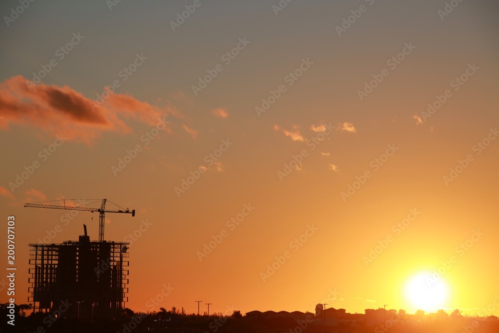 Skeleton of Building with Crane Scaffolding Under Construction at Sunset with Mostly Clear Sky a Few Scattered Orange Clouds