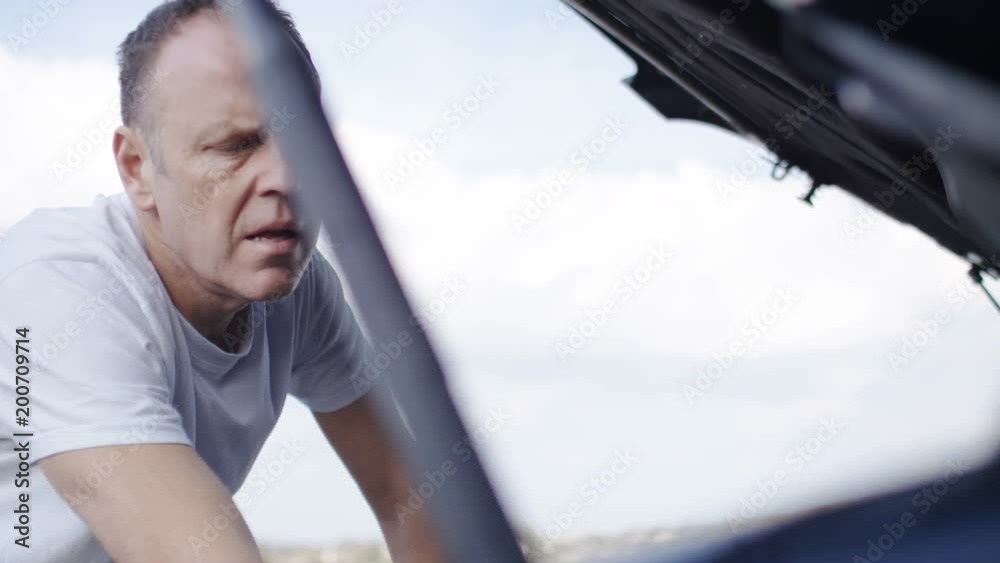 Middle aged man checking the car engine during a breakdown