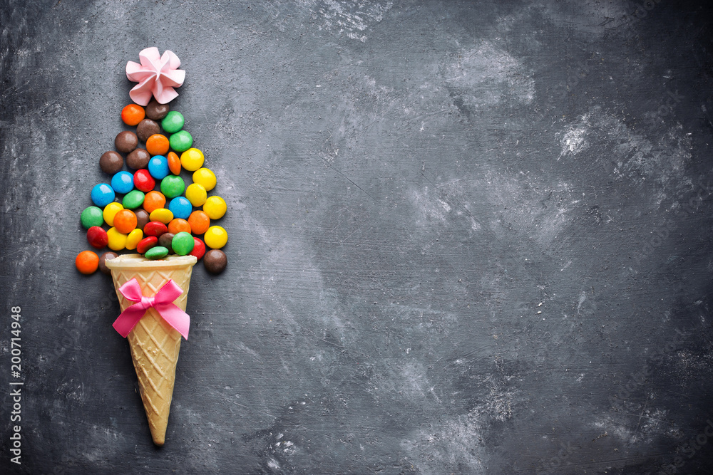Ice cream cone with colorful chocolate glaze candy dragee on dark concrete background