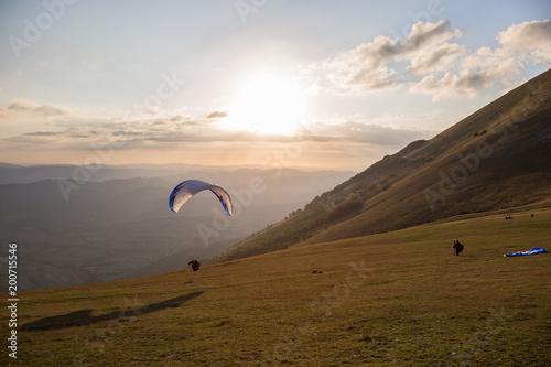 A paraglider taking off from Monte Cucco (Umbria, Italy),at almost sunset, with people watching photo