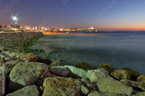 Nocny widok zatoki Morza Śródziemnego, umocnionego brzegu i nocnych świateł w Tel Awiwie, Izrael, w oddali widoczna rozświetlona Jaffa