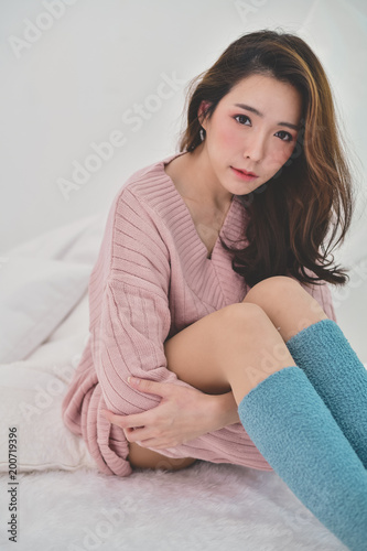 Winter Concept. Cute Asian girl in winter dress. Beautiful woman is relaxing in a white bedroom. Beautiful women in winter clothes are relaxing in the morning. 