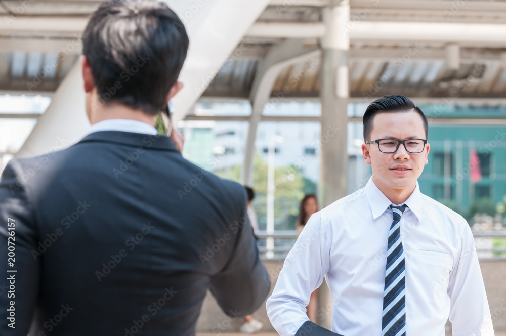 Young Asian businessman wearing glasses and white shirt walking through a business man who talking to someone with smartphone in middle city town.